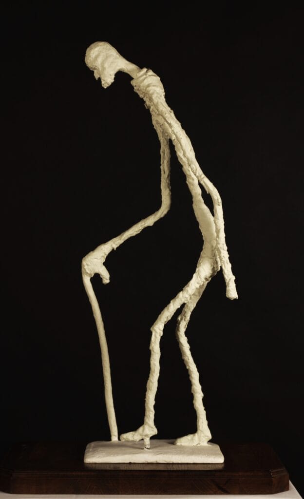 A sureal sculpture of an elongated figure of an old man with a cane created by Valeriu Cazacevschi inspired by the sculptor Giaccometti